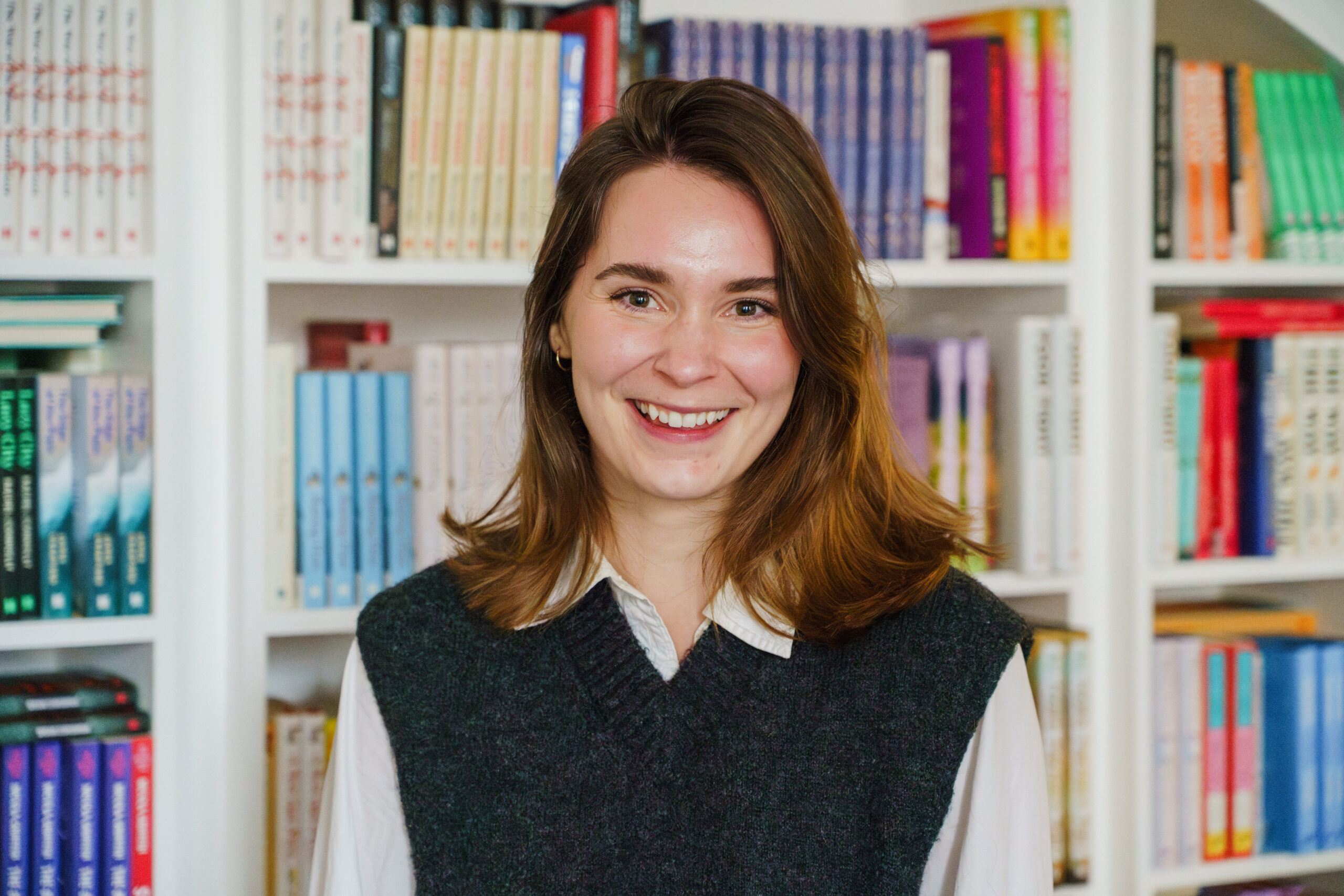 A photograph of Sasha Cox in front of some bookshelves